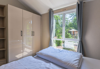 Bedroom in Forest Cottage at Recreatiepark de Paalberg, Netherlands, with window view of lush forest and cabin.