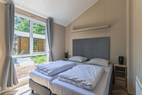Schlafzimmer im Forest Cottage im Recreatiepark de Paalberg, Niederlande, mit Doppelbett und großem Fenster.
