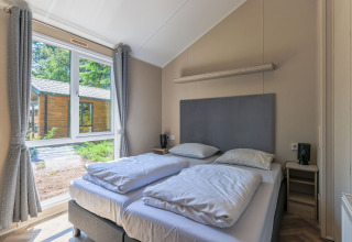Schlafzimmer im Forest Cottage im Recreatiepark de Paalberg, Niederlande, mit Doppelbett und großem Fenster.