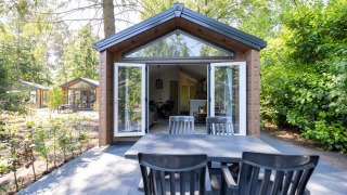 Buiten eettafel voor een boscottage met open deuren bij Recreatiepark de Paalberg in Nederland.