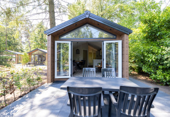 Espace repas extérieur devant un chalet forestier aux portes ouvertes à Recreatiepark de Paalberg, Pays-Bas.
