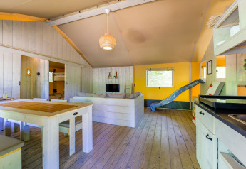 Indretning af Glamping-telt på Recreatiepark de Paalberg i Holland med sofa, spisebord og rutsjebane.