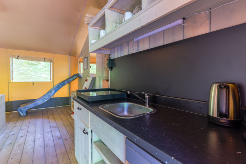 Interior de la Glamping Tent en Recreatiepark de Paalberg, Países Bajos, con cocina y tobogán azul.