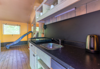 Interior de la Glamping Tent en Recreatiepark de Paalberg, Países Bajos, con cocina y tobogán azul.