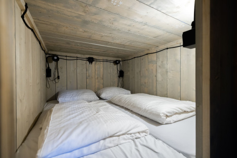 Acogedora zona de dormir con paredes de madera y cuatro almohadas en una tienda glamping de Paalberg.