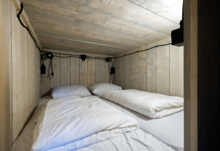 Knusse slaapruimte met houten wanden en vier kussens in een glamping tent op Recreatiepark de Paalberg.