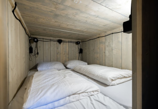 Acogedora zona de dormir con paredes de madera y cuatro almohadas en una tienda glamping de Paalberg.