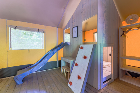 Interior de una tienda glamping con tobogán, pared de escalada y área de dormir en Recreatiepark de Paalberg.