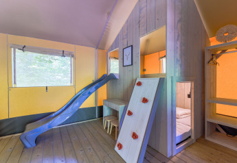 Interior de una tienda glamping con tobogán, pared de escalada y área de dormir en Recreatiepark de Paalberg.
