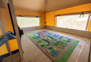 Interior de una tienda glamping en Recreatiepark de Paalberg, Países Bajos, con una alfombra de juegos.