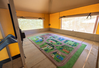 Intérieur d’une tente glamping au Recreatiepark de Paalberg, Pays-Bas, avec tapis de jeu et grandes fenêtres.