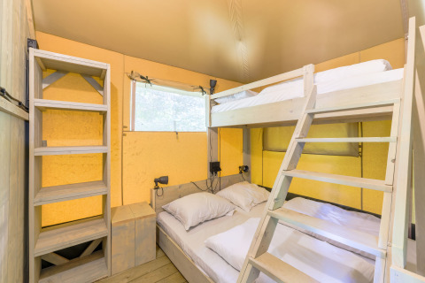 Interior de tienda glamping en Recreatiepark de Paalberg, Países Bajos, con litera y estantería de madera.