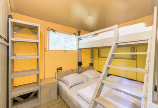 Interior de tienda glamping en Recreatiepark de Paalberg, Países Bajos, con litera y estantería de madera.