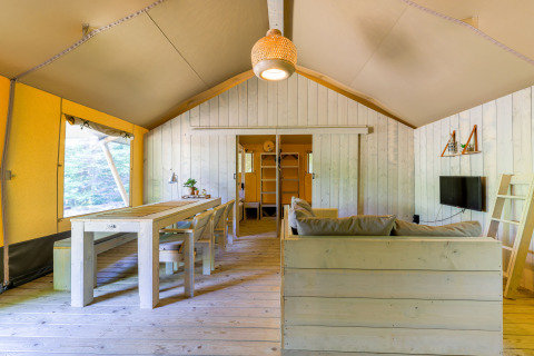 Interno di una spaziosa tenda glamping al Recreatiepark de Paalberg nei Paesi Bassi, con arredi in legno chiaro.