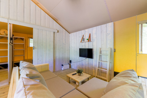 Bright living area inside a glamping tent at Recreatiepark de Paalberg with sofa, table, and TV.