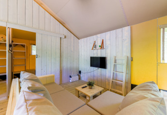 Sala luminosa en una tienda glamping en Recreatiepark de Paalberg con sofá, mesa y televisor.