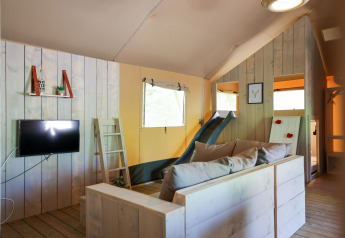 Vista interna di una tenda glamping con pannelli in legno, divano, TV, scala e scivolo.