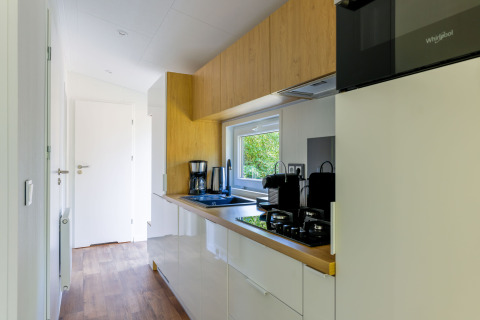 Cocina moderna de casa pequeña con armarios blancos y toques de madera en Recreatiepark de Paalberg, Países Bajos.