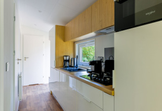 Cocina moderna de casa pequeña con armarios blancos y toques de madera en Recreatiepark de Paalberg, Países Bajos.