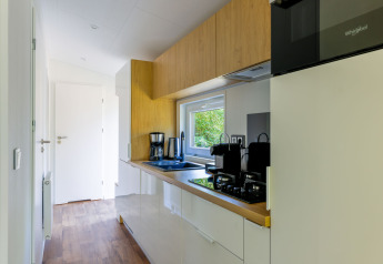 Modern tiny house kitchen with white cabinets, wood accents, and window at Recreatiepark de Paalberg, Netherlands.