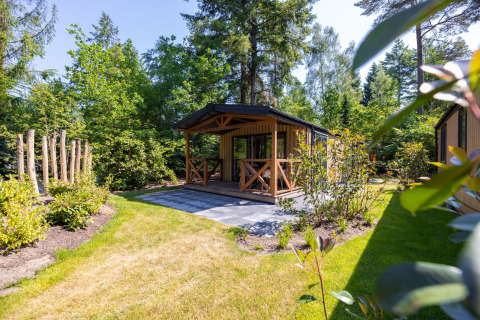 Acogedora tiny house Heide Lodge con porche, en un frondoso jardín verde rodeado de árboles altos.