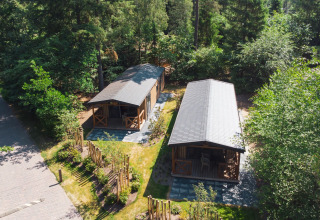 Vista aérea de dos tiny houses en Heide Lodge, Recreatiepark de Paalberg, Países Bajos, rodeados de árboles.