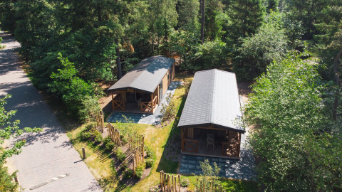 Vista aérea de dos tiny houses en Heide Lodge, Recreatiepark de Paalberg, Países Bajos, rodeados de árboles.
