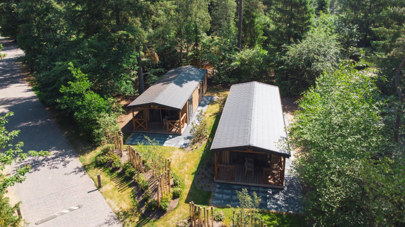 Vista aérea de dos tiny houses en Heide Lodge, Recreatiepark de Paalberg, Países Bajos, rodeados de árboles.