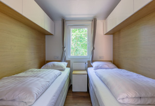 Two single beds in a small, bright bedroom with window and wood view at Heide Lodge in the Netherlands.