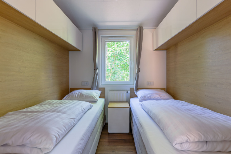 Zwei Einzelbetten in einem kompakten, hellen Schlafzimmer mit Fenster auf Heide Lodge in den Niederlanden.
