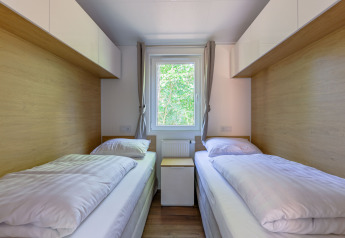 Dos camas individuales en un dormitorio pequeño y luminoso con ventana en Heide Lodge en los Países Bajos.