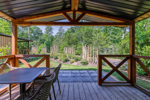 Uitzicht vanaf houten veranda bij Heide Lodge in Recreatiepark de Paalberg, met tuin en bos op de achtergrond.
