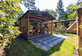 Charming Heide Lodge tiny house at Recreatiepark de Paalberg in the Netherlands, featuring a porch and garden.
