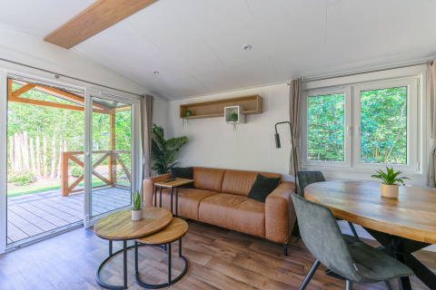Acogedora sala de una tiny house en Heide Lodge, Recreatiepark de Paalberg, con vista al exterior natural.