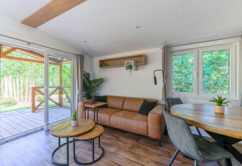 Acogedora sala de una tiny house en Heide Lodge, Recreatiepark de Paalberg, con vista al exterior natural.
