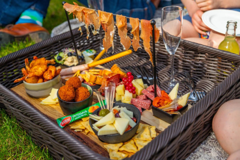 Picnic all'aperto in un glamping di parco vacanze con cestino di tapas, formaggi, prosciutto e snack vari.