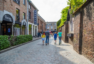 Een familie wandelt door een kasseistraat bij een vakantiepark met glampingaccommodaties.