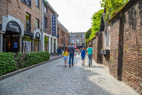 Een familie wandelt door een kasseistraat bij een vakantiepark met glampingaccommodaties.