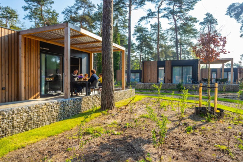 Familia disfruta del glamping en un parque vacacional con cabañas modernas de madera y naturaleza.