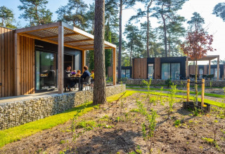 Gezin geniet van glamping in een vakantiepark met moderne houten chalets in een bosrijke omgeving.