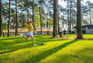 Due bambini giocano a calcio su un prato circondato da alberi e tende glamping in un villaggio vacanze.