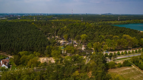 Vista aérea de un parque vacacional con alojamientos glamping en un entorno boscoso junto a un lago.