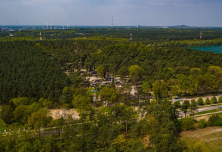 Vue aérienne d’un parc de vacances proposant du glamping au cœur d’une forêt, près d’un lac.