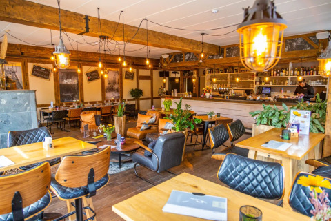 Acogedora cafetería en parque de vacaciones glamping con muebles de madera, plantas y luz cálida.