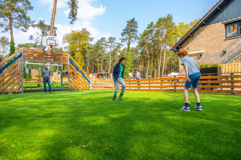 Tres personas juegan fútbol en un campo verde en un parque vacacional con opciones de glamping en la naturaleza.