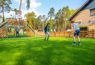 Drie personen spelen voetbal op het gras van een vakantiepark met glamping in een bosrijke omgeving.