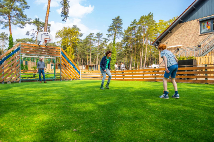 Drei Menschen spielen Fußball auf einer Wiese in einem Ferienpark mit Glamping-Angeboten im Wald.