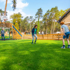Drei Menschen spielen Fußball auf einer Wiese in einem Ferienpark mit Glamping-Angeboten im Wald.
