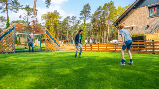 Drei Menschen spielen Fußball auf einer Wiese in einem Ferienpark mit Glamping-Angeboten im Wald.