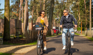 Dos personas montan bicicleta por un parque de vacaciones rodeado de árboles y alojamientos glamping.